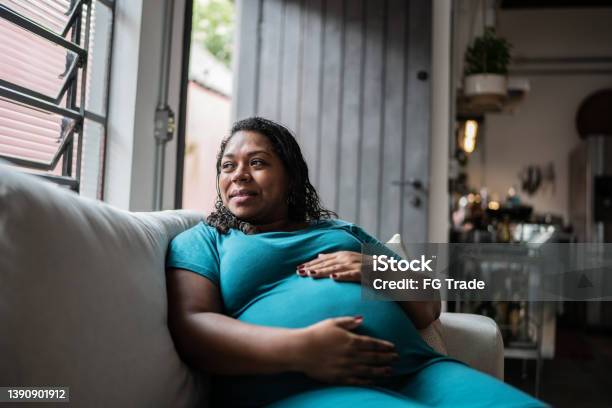 Pregnant Woman Touching Her Belly And Contemplating At Home Stock Photo - Download Image Now
