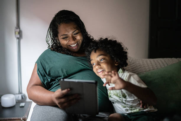 мама и сын с помощью цифрового планшета лежат дома на кровати - human pregnancy african ethnicity women family стоковые фото и изображения