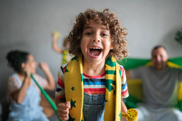 ritratto di un ragazzo che tifa per la squadra di calcio brasiliana con la famiglia a casa - little boys people indoors soccer foto e immagini stock