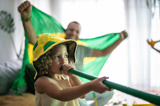 Girl with a vuvuzela with her family cheering Brazilian soccer team at home