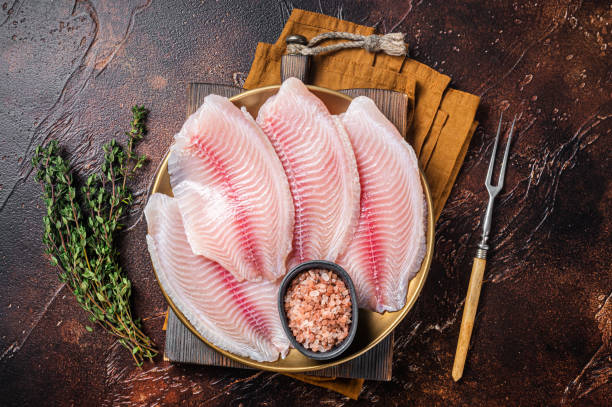 filetto di pesce crudo di tilapia in un piatto con spezie. sfondo scuro. vista dall'alto - bistecca di filetto foto e immagini stock