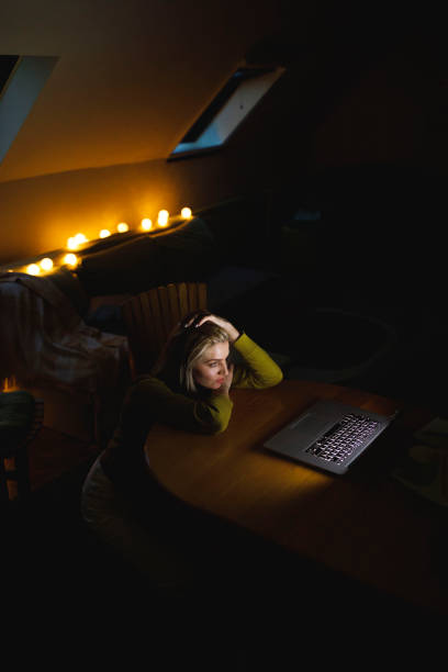 Woman watching a suspenseful movie on laptop late at night High angle view of mid adult woman sitting on the floor, resting her hands and head on the coffee table while watching a suspenseful movie on laptop, late at night. suspenseful stock pictures, royalty-free photos & images