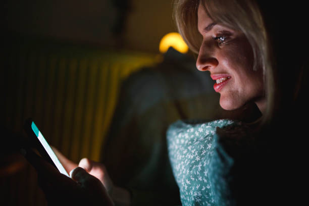 istock Profile view of smiling woman using smart phone while relaxing late at night 1390905946