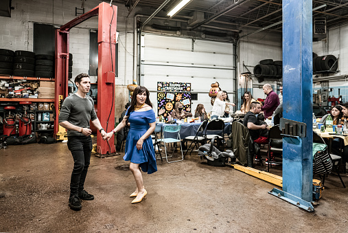 Mexican  couple dancing at the fiesta birthday party. They are wearing casual clothes. Interior of car and motorcycle repair shop with party decoration at night.