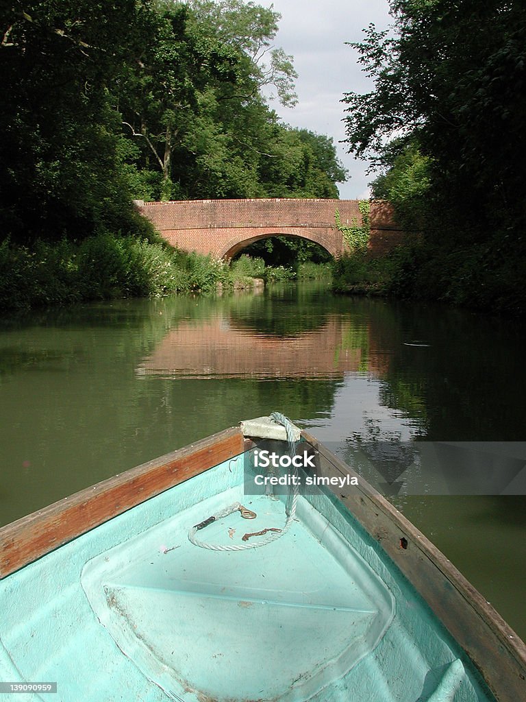 Lazy boat trip Lazy summer afternoon boat trip down Basingstoke Canal, Southern England. Photo shows a boat headed down a canal torwards a brick bridge on a sunny summers day. The bridge is reflected in the water. Aquatic Sport Stock Photo