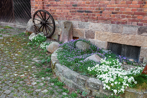 A small flower bed is paved with stones with flowers in the old style