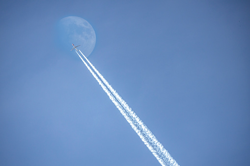 Vapor trail from airplane that is passing underneath the moon