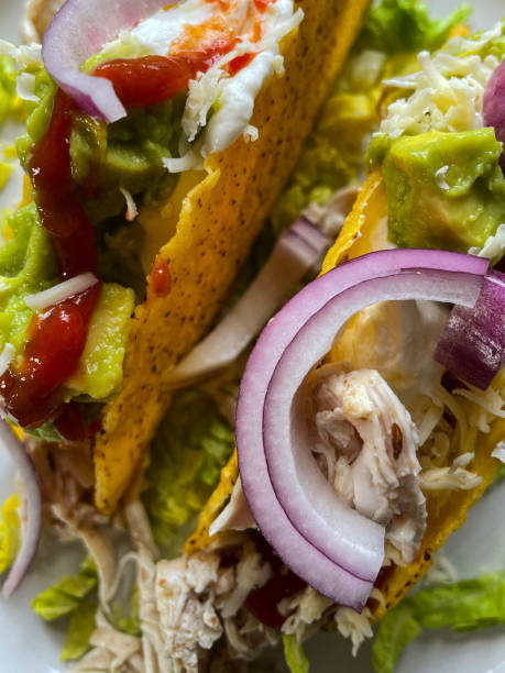 istock Full frame image of taco shells filled with roast chicken, tomato salsa, guacamole, shredded lettuce, red onion, sour cream and grated cheese on dinner plate, elevated view 1390914376