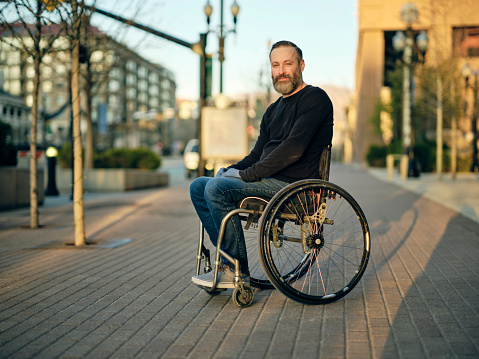 A disabled man in a wheelchair, in the downtown area of a city.