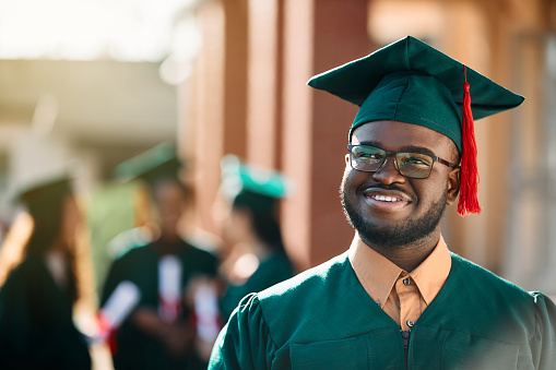 Happy African American student day dreaming on his graduation day and looking away.