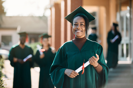 Portrait of happy African American female student with graduation diploma looking at camera.