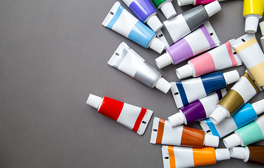 Tubes with acrylic paint in different colors on grey background, the concept of creativity, drawing and art.
