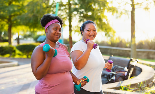 Two multiracial women exercising in the city. They are mature, plus size women, staying in shape together, running, jogging or power walking side by side, with hand weights. The African-American woman is in her 40s. Her Pacific Islander friend is in her late 30s.