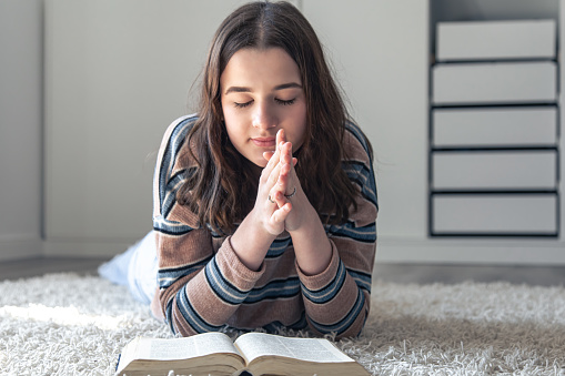 A young woman reading the bible lying on the floor, the concept of faith in God, religion, christian spiritual life.