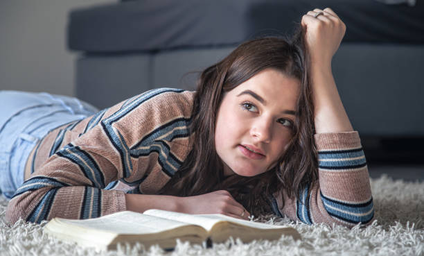istock A young woman reading a book while lying on the floor at home. 1390921788