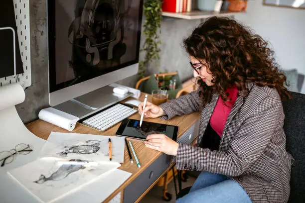 Graphic designer woman using computer drawing board for illustrating in her office. Sitting at the table, drawing a new project.