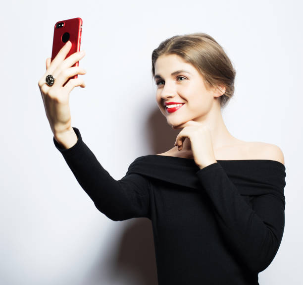 istock Selfie time. Young smiling blond woman doing selfie on white background 1390925296