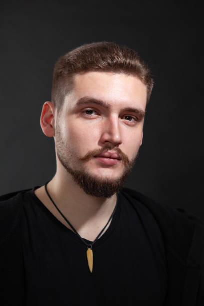 Close-up studio portrait of a 22 year old bearded man on a black background