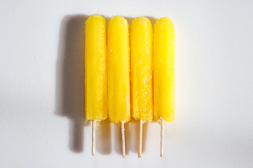 four yellow banana-flavored popsicles on a white background