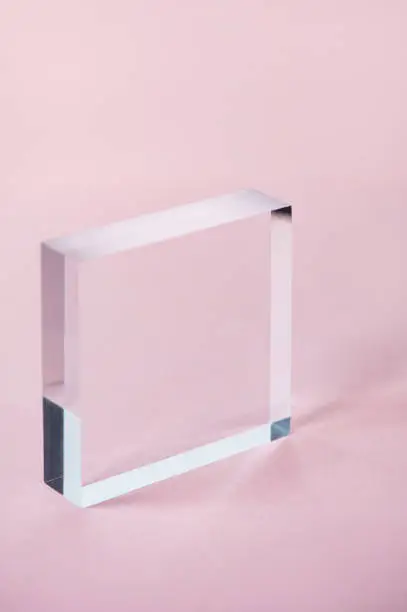 Acrylic Solid Display Block for Shop Windows on pink background, empty podium for product presentation, geometric stand for cosmetics