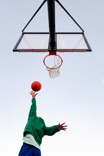 unrecognizable latin woman shooting in a basketball hoop seen from below with the sky in the background, concept of urban sport outdoors, copy space for text
