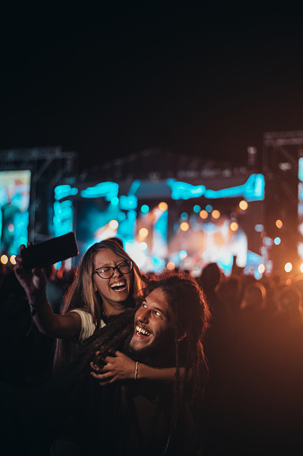 Romantic couple having fun on a music festival and using smartphone while posing for a selfie. Love and celebration concept.