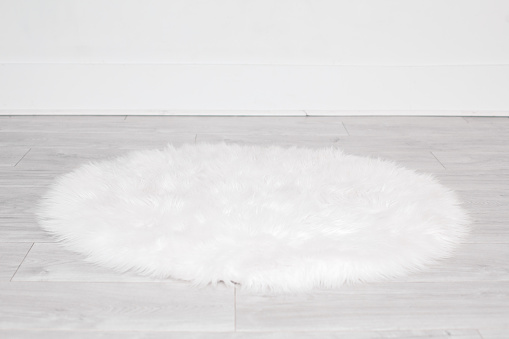 White round fluffy rug carpet lying on floor by white wall at home. Background mockup for designs and backdrop.