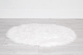 White round fluffy rug carpet lying on floor by white wall at home. Background mockup for designs and backdrop