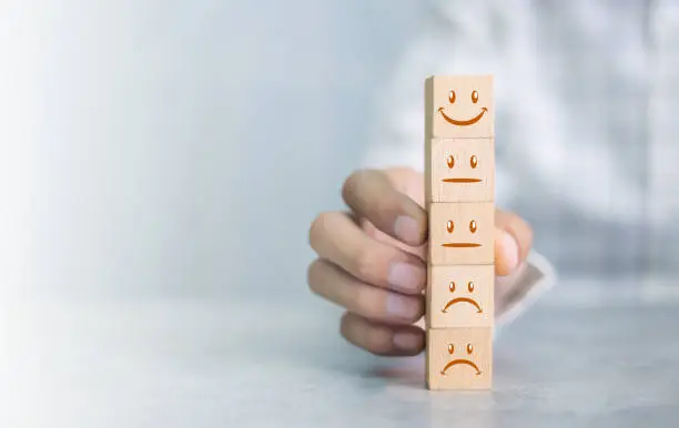 Photo of Close up customer hand choose smiley face icon on wood cube, Service rating, satisfaction concept.