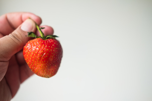 Hand holding red strawberry, close up