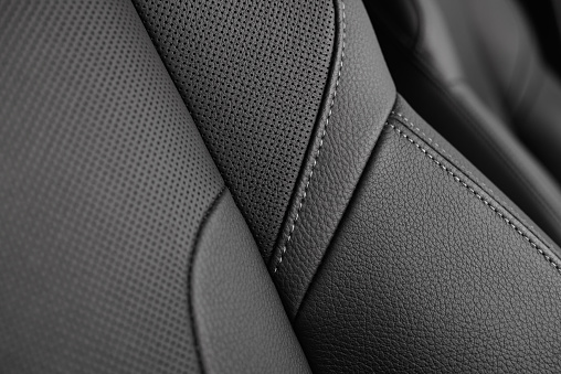 Closeup of a perforated leather seat with stitching detail in a modern sporty car.  Shallow focus.  Monochromatic.