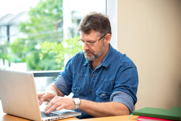 istock Freelance work. Casual dressed man sitting at wooden desk inside garden working on computer pointing with color pen electronic gadgets dropped around on table side view 1390969383