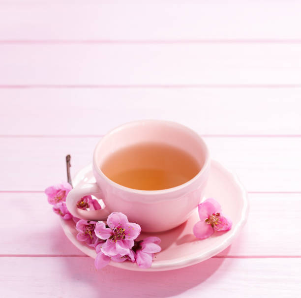 istock Cup of tea and spring  flowers  (Peach blossom) on light pink wooden table. Selective focus 1390972458