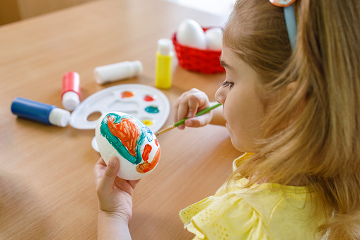 Young girl using colors and coloring brush when coloring Easter eggs