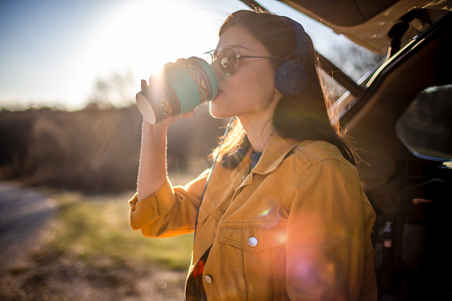 Beautiful woman resting in a car trunk with coffee during her road trip
