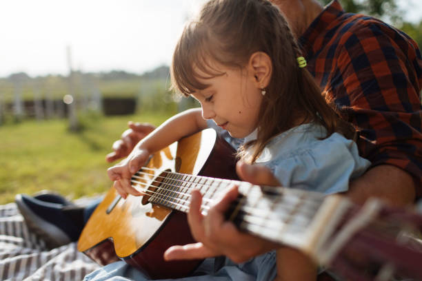 Cropped photo of young girl playing guitar together with her grandpa