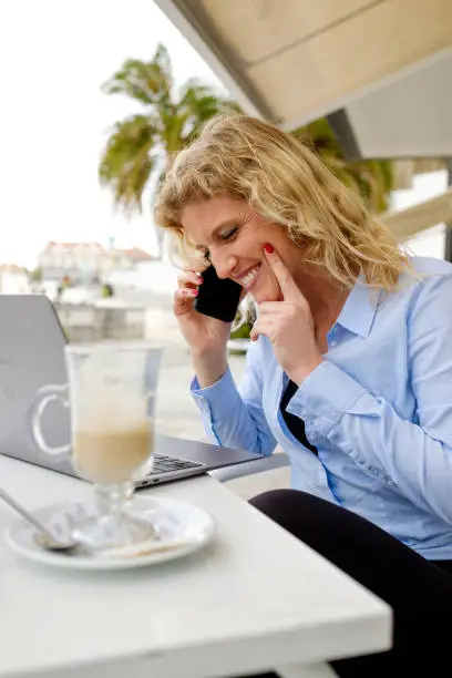 Woman working from a beach terrace, on a smartphone call, digital nomad