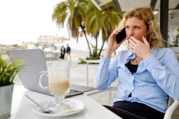Woman working from a beach terrace, on a smartphone call, digital nomad