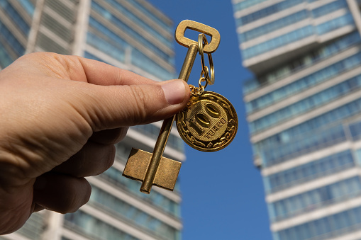 Golden key with a keychain in the form of 100 Kazakhstani tenge on the background of a modern building