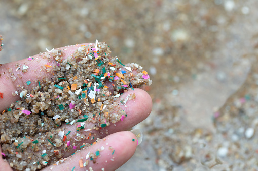 El primer plano lateral de las manos muestra residuos microplásticos contaminados con la arena del mar. Los microplásticos están contaminados en el mar. Concepto de contaminación del agua y calentamiento global. photo
