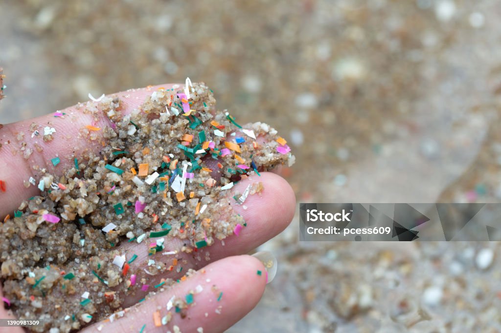 Close-up side shot of hands shows microplastic waste contaminated with the seaside sand. Microplastics are contaminated in the sea. Concept of water pollution and global warming. Microplastic Stock Photo