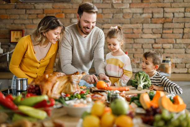 szczęśliwi rodzice i ich dzieci przygotowujące posiłek na święto dziękczynienia. - roast turkey turkey cutting roasted zdjęcia i obrazy z banku zdjęć