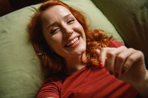 Directly above shot of young woman smiling at camera as if she is taking a selfie Headshot of cheerful young redhead lying on back, on her cozy sofa, looking and smiling at camera as if she is taking a selfie or talking via video call. man video call pov stock pictures, royalty-free photos & images