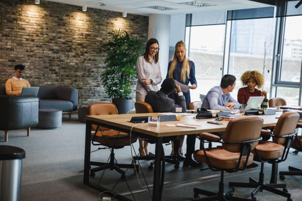 Group of diverse young business people having a project briefing in a modern office space Wide shot of diverse group of young people hanging out, chatting and collaborating on projects in a modern, open plan office space. wide shot stock pictures, royalty-free photos & images
