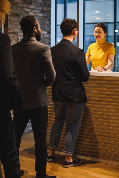 People waiting in line in front of receptionist at the office lobby Full length shot of small group of business people standing in line, waiting to be hosted by a charming female receptionist at the front desk of a modern office space. hotel reception hotel business lobby stock pictures, royalty-free photos & images