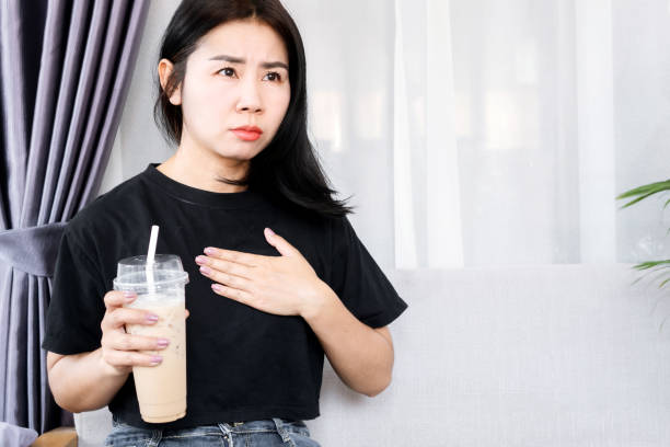 la mujer asiática tiene problemas con los latidos del corazón más rápido después de beber café, palpitaciones del corazón causadas por el concepto de cafeína - sistema de conducción cardíaco fotografías e imágenes de stock