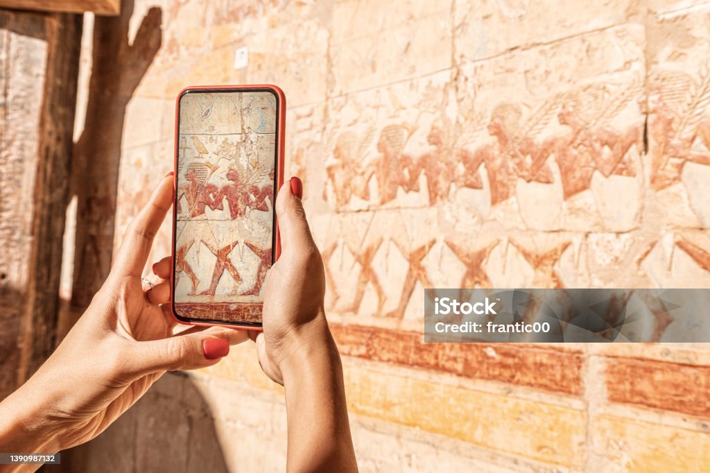 Travel blogger girl takes pictures on a smartphone at the famous Hatshepsut temple frescoes in the ancient city of Luxor in Egypt. Or using visual tourist guide Luxor - Thebes Stock Photo