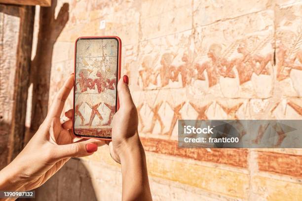Travel Blogger Girl Takes Pictures On A Smartphone At The Famous Hatshepsut Temple Frescoes In The Ancient City Of Luxor In Egypt Or Using Visual Tourist Guide Stock Photo - Download Image Now