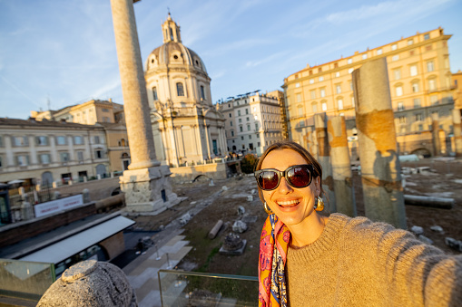 Happy woman taking selfie photo on the background of Roman forum. Style caucasian woman in dress and shawl in hair having fun traveling italian landmarks