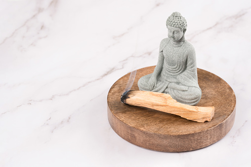 Burning palo santo sticks with Buddha statue in a meditation room on white marble background. Zen concept, meditation and spiritual practices. Mental health